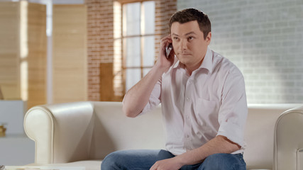 Handsome man discussing business issue in phone call with partner, home interior