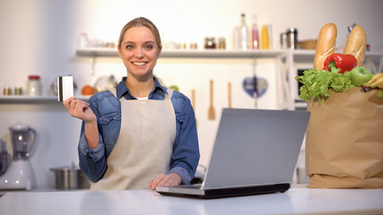 Smiling woman holding credit card in kitchen, food purchase and delivery online