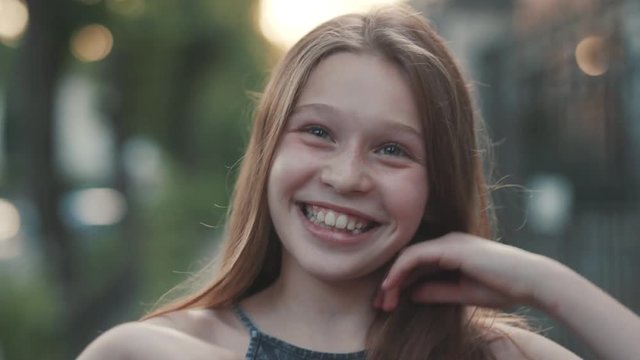 Close-up shooting of attractive young green-eyes girl. Teenage girl in green clothes laughing to tears. Outdoors. Summertime. Green blurred background.