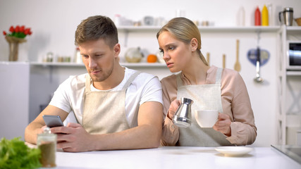 Miserable wife peeping at husband phone, male texting with lover, betrayal