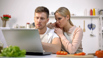 Upset couple reading food recipes on internet, having troubles with cooking