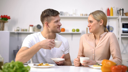 Loving couple communicating at kitchen, holding coffee cup, time together