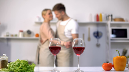 Wine glasses standing on table, loving couple dancing on background, romance