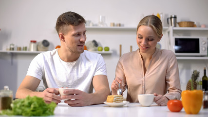 Loving couple having tea and communicating at kitchen, eating cake, happiness