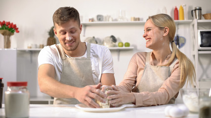 Happy couple clumsily kneading dough, spending fun time together in kitchen