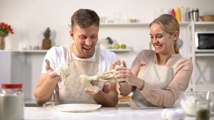 Carefree couple clumsily kneading dough, having fun in kitchen, inept chefs