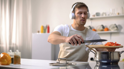 Handsome male in headphones cooking dinner, homemade healthy food, nutrition