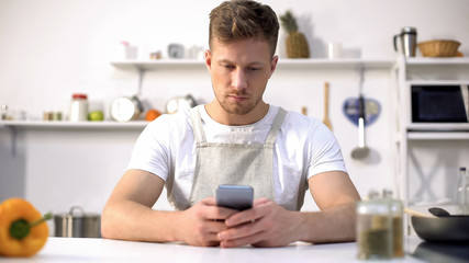 Handsome man in apron looking for culinary recipe in internet, kitchen novice