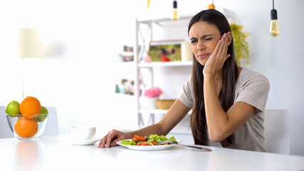 Woman eating salad, feeling tooth ache from excess acid in products, health