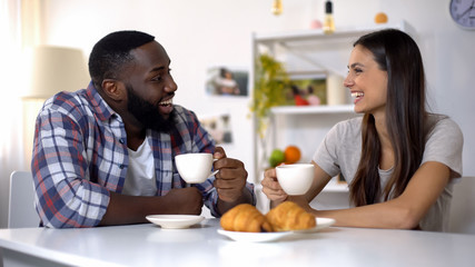 Mixed-race couple talking and laughing during breakfast at home, morning coffee