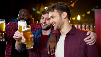 Drunk multiethnic friends clinking beer glasses, spending time in pub, party
