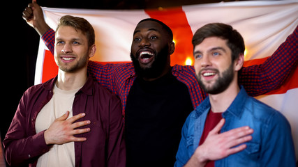 Caucasian and black male friends singing national anthem, waving english flag