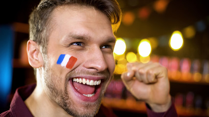 Joyful french fan with painted flag celebrating team victory, making yes gesture