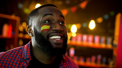 Extremely happy black spanish fan with flag on cheek shouting, team winning