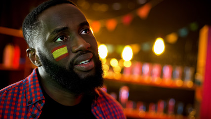 Black spanish football fan with flag on cheek disappointed, national team losing