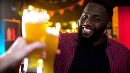 Cheerful african-american male clinking beer glass, enjoying results time in bar