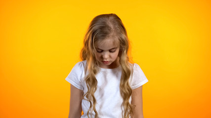 Blond curly girl looking down isolated on orange background, feeling guilty