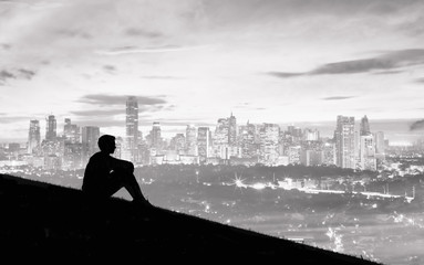 Man sitting on hill top overlooking the city. 