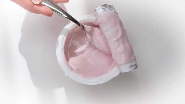 Woman's hand holding a spoon of yogurt from a plastic cup. The concept of yogurt as food and health care. Top view. Slow Motion