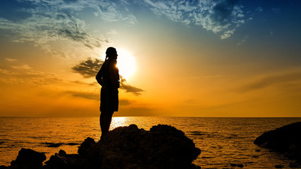Silhouette of a man standing on the rock at the beach on sunset time