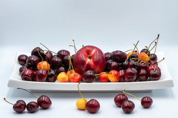Cherries and peach on a restangular plate. Fruit on a white background.