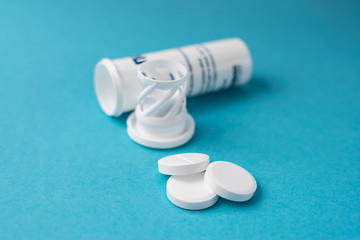 Big white tablets and plastic container isolated on blue background. Health care and treatment concept.