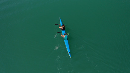 Aerial drone top view of sport canoe operated by 2 young fit athletes in tropical lake with clear water