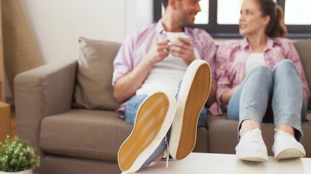 moving, people and leisure concept - feet of couple couple sitting on sofa and drinking coffee at new home