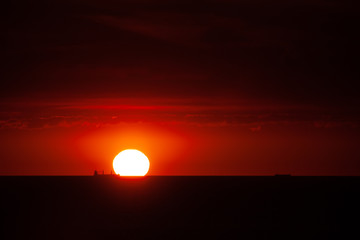 Boat traffic in the sunset on the North Sea. The sun touches the sea in the harbor entrance of Rotterdam.Silhouette of ships in front of glowing red background.