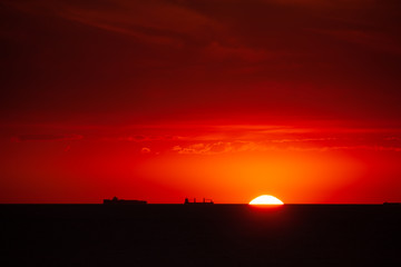Fototapeta na wymiar Waterway. Boat traffic in the sunset on the North Sea. The sun touches the sea in the harbor entrance of Rotterdam.Silhouette of ships in front of glowing red background.