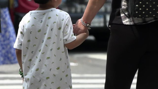Little boy holding mother hands waiting to cross street