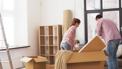 accommodation, repair and real estate concept - happy couple with stuff in cardboard boxes moving to new home, unpacking things and arranging room - Powered by Adobe