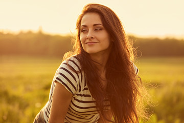 Fototapeta premium Beautiful calm smiling young woman looking happy with long bright long hair on nature bright sunset summer background. Closeup