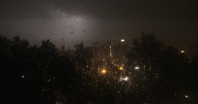 Thunderstorm in city, raindrops at window with lightnings in background