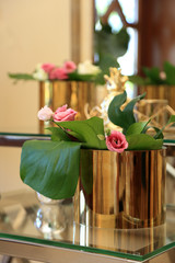 Piękna dekoracja z kwiatów i złotej donicy na szklanym stoliku przed lustrem.	