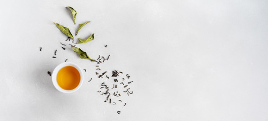 Tea concept with white teacup surrounded with fresh tea leaves on concrete background with copy...