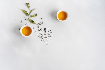 Tea concept with white tea set of cups and teapot surrounded with fresh tea leaves on concrete background with copy space.