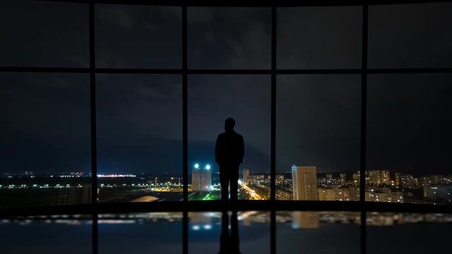 The man standing near the window on the city lightning background. time lapse