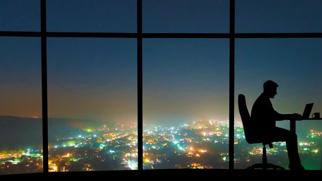 The man working near a window on a night city background. time lapse