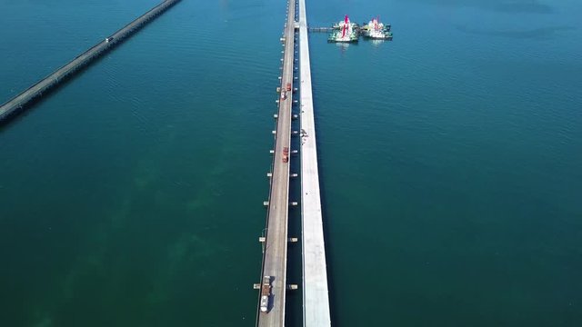 Aerial view, cargo trailer driving on the long bridge above ocean to commercial port for transport goods. Titl up shot.