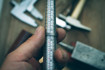 hand of a goldsmith measures a ring on a sizer gauge, jeweler steel sizing tool against a dark...