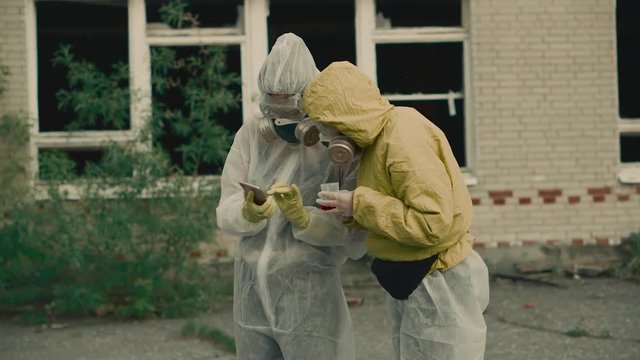Two scientists put on a respirator and conduct research. The environment is in danger. Two girls in protective suits from radiation. Enter the data into the phone.