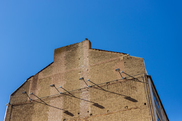 Exterior low angel of elevated old rough refractory naked brick wall facade with hanging lamp and its shadow at the side of apartment building against deep blue sky. Typical character brick building.