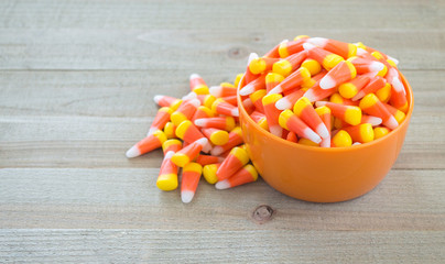 small orange bowl overflowing with colorful candy corn on a wood background with copy space