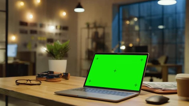 Mock-up Green Screen Stanting on the Desktop. In the Background Stylish Modern Office Studio in the Evening with Big Cityscape Window