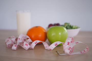 Focus at measuring tape - Healthy food with vegetable salad, orange, apple and milk. Concept Diet