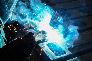 The worker is engaged in carrying out close-up welding work with the help of electric arc welding at his workplace.