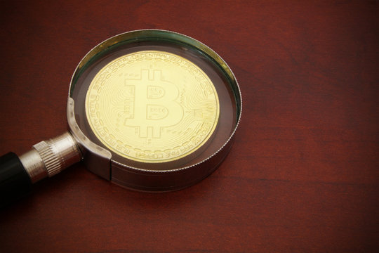 Magnifying glass and golden bitcoin close up