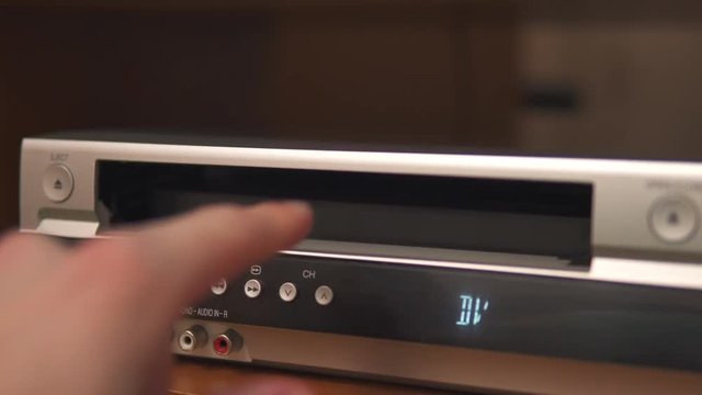 Hand insert old VHS cassette in silver videorecorder