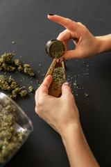 Woman preparing and rolling marijuana cannabis joint. Close up of marijuana blunt with grinder....